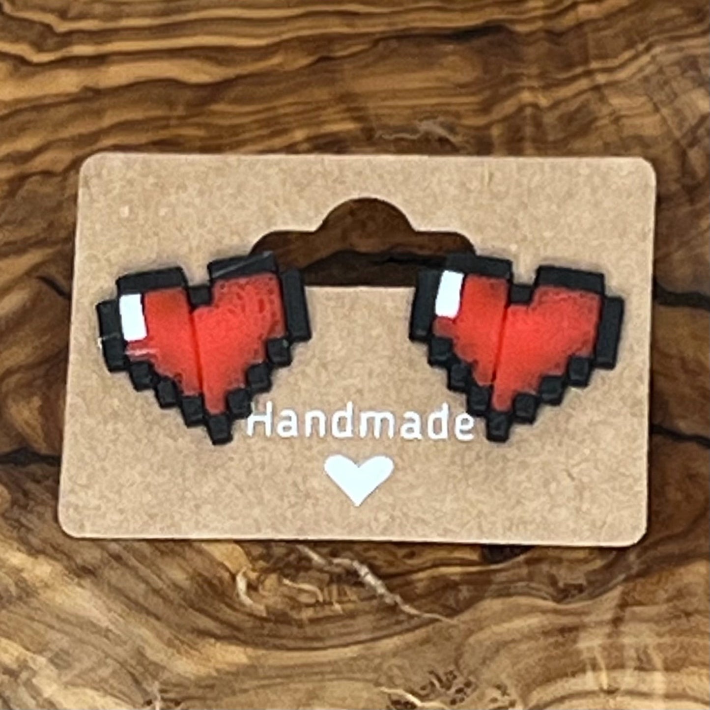 Pixel heart-shaped earrings on a 'Handmade' card against a wooden background