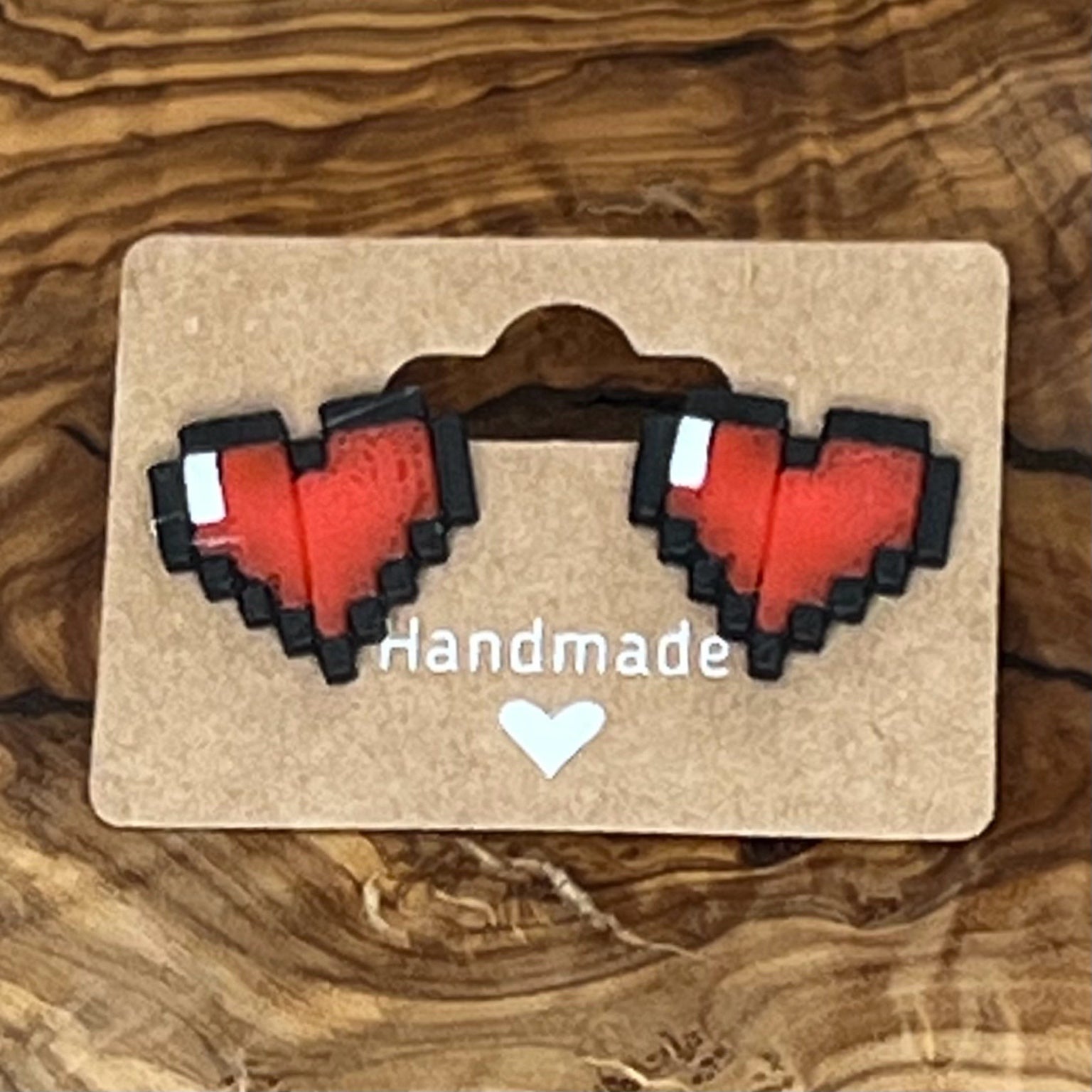 Pixel heart-shaped earrings on a 'Handmade' card against a wooden background