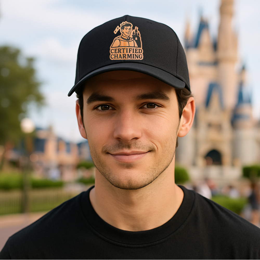 Man wearing a black cap with 'Certified Charming' text and logo in front of a blurred castle background