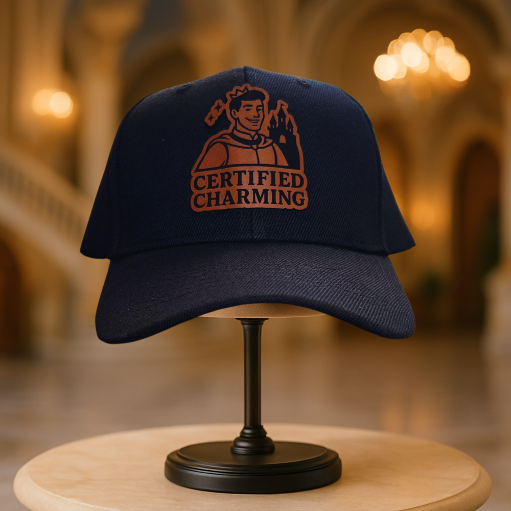 Black cap with 'Certified Charming' logo on a wooden stand with a blurred background