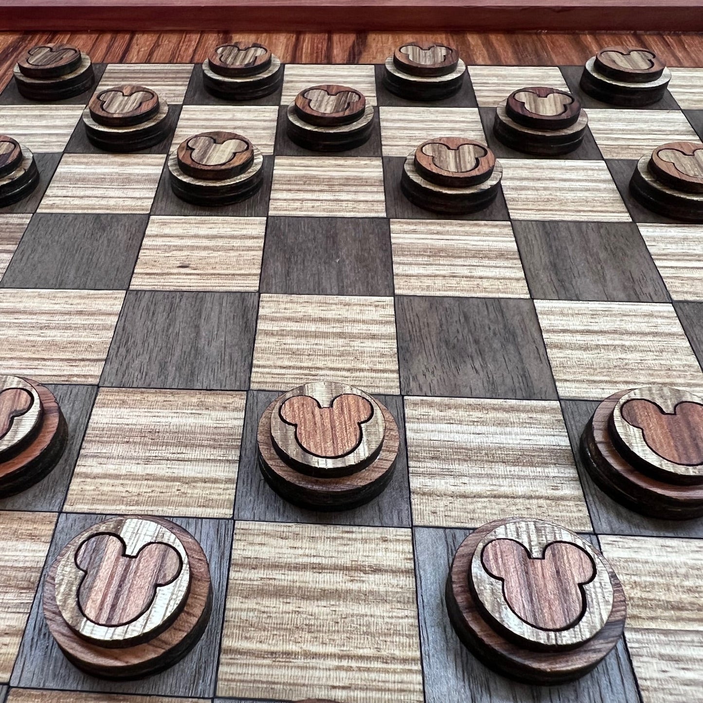 A luxury handcrafted checkerboard made from exotic woods with a pattern of squares in shades of walnut, cherry, redwood, and zebrawood, accompanied by matching round game pieces.